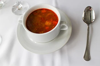 goulash soup in a small round white bowl with a spoon placed on the right