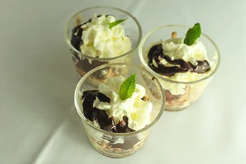 3 shot glass desserts: Sponge cake with vanilla sauce, chocolate sauce and whipped cream, each decorated with a leaf of lemongrass