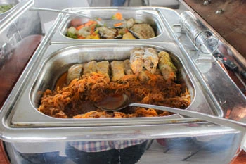 rolls of stuffed cababge with shredded, cooked cabbage tinted pink with paprika in a stainless container