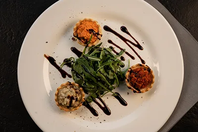 3 patry cups filled with various spreads rranged in a triangle on a white plate with rocket salad in the middle