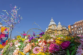 a top of the yellow building in Városháza Park, Budapest during the Spring & Easter market. Colourful flower installation and a maypole in the foreground.