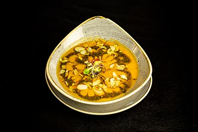 Creamed sweet potato soup withparsley pesto and almond slices in a beige oval bowl