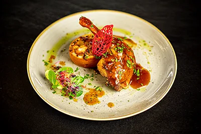 Roasted duck leg with gravy and cabbage noodles in chimney cake on a round beige plate