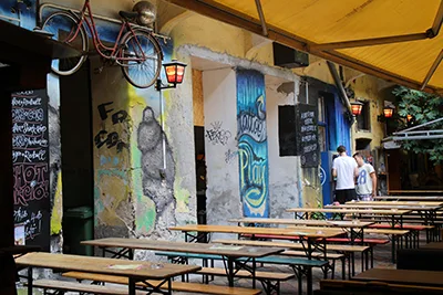 the painted art on the walls of Füge Ruin Bar, two men in white T-shirts talking in the background next to the long wooden benches and tables