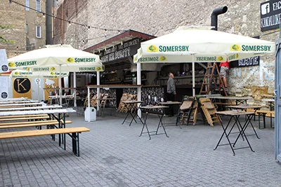 courtyard of the Kandallokert garden pub, with white shades and wooden benches and tables