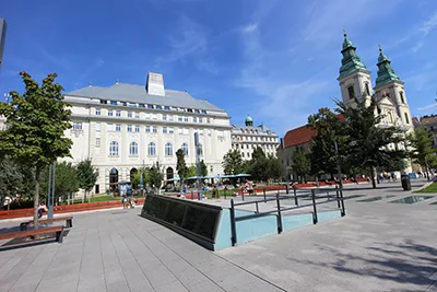 the off-white facade of a resturant and the two towers of the inenr city church on the square