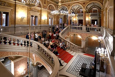 guided tour guests sitting on the red carpeted main stair of the Hungarian Opera House