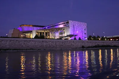 The Palace of Arts/MüPa building illuminated in purple at night. Photo was taken from a ship on the Danube