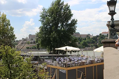 white wooden chairs under a large, white umbrella shade at the terrace of Raqpart on the Pest riverbank