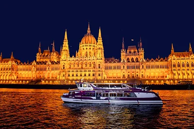 a small catamaran excursion boat on the Danube in Budapest at night, the illuminated Parliament in the background