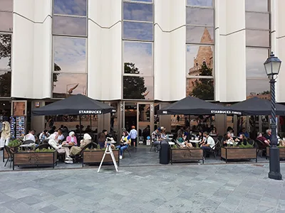 the terrace of the Starbucks Buda Castle cafe, patrons sitting at wooden tables under black shades