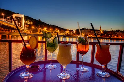 5 cocktails arranged on a small table on the deck of a cruise boat, after sunset,