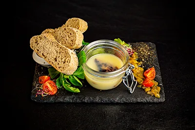 foie gras in its own fat served in a glass jar with slices of whole bread and veggies