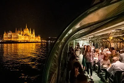 part of a panorama cruise catamaran on the Danube in Budapest at night. Guests are strolling on the open deck.