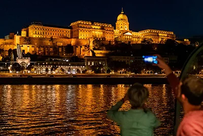 guests on a cruise boat taking photos of the illuminated Buda Castle at night