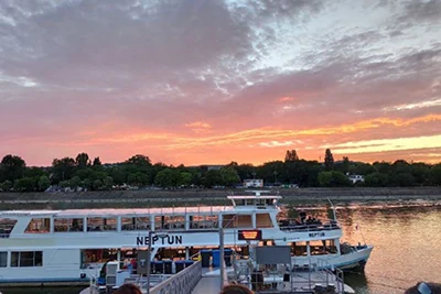 a white cruise boat named Neptun moored in the dock on the Danube in Budapest at sunset