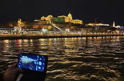 View of the lit up Buda Castle buildings at night as seen from a boat on the Danube