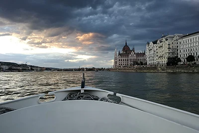 photo taken from the front of a cruise ship on a cloudy day, the Parliament can be see further down on the riverbank