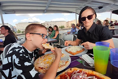 son eating his ham and corn pizza and me having a langos on a river cruise in Budapest
