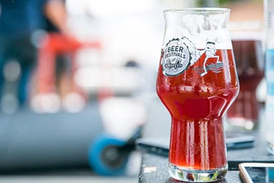 red, sour cherry beer in a tasting glass with the festival logo in white and black on its side