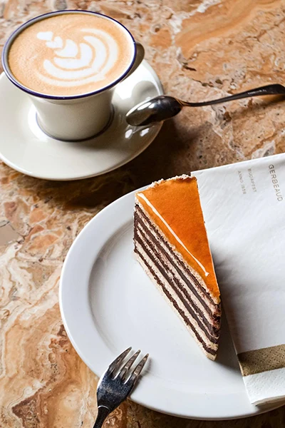 a slice of Dobos cake and a cup of cappuccino wih latte art