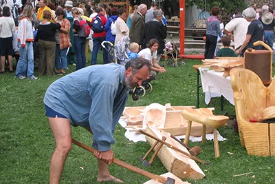 a middle-aged bearded man carving wood with an ax - Festival of folk arts in Budapest