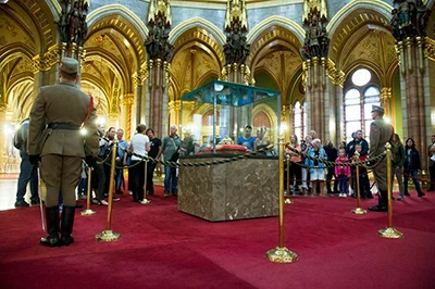 2 soldiers standing next to the Holy crown displayed in a glass cabinet in the Hungarian Parliament, visitors viewing the crown