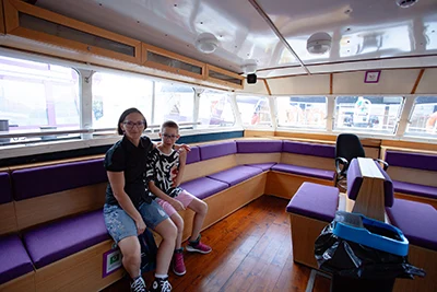My son and I sitting on the purple upholstered sofa bench onboard the Margitsziget cruise boat in Budapest