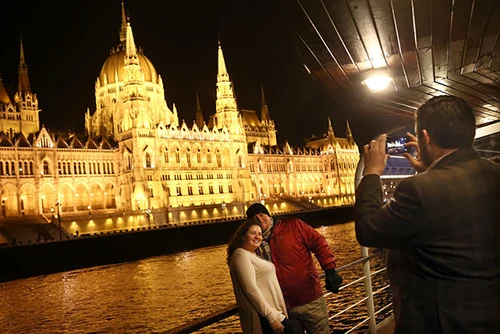 a couple being photographed by a man on cruise ship in Budapest, the illuminated Parliament in the background