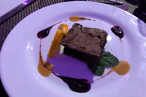 a square slice of brownie with salted caramel on a white round plate