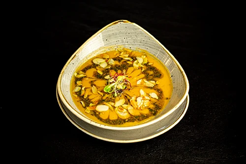 sweet potato cream soup sprinkled with almond slices, green pesto served in an oval, beige colored bowl