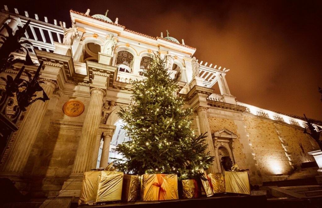 a large Christmas tree surrounded with gift boxes in front of the palace building in Castle Bazaar