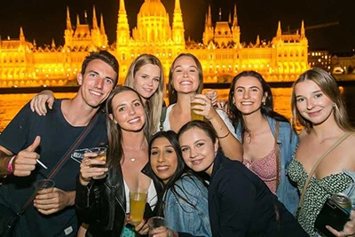 half a dozen young people possibly on a boat party in Budapest, the illuminated Parliament building in the background
