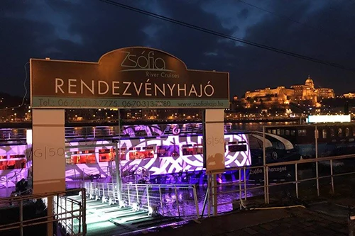 The ramp leading to the entrance of the Zsófia Party Boat in Budapest, Buda Castle illuminated for the night in the right sid eof the photo