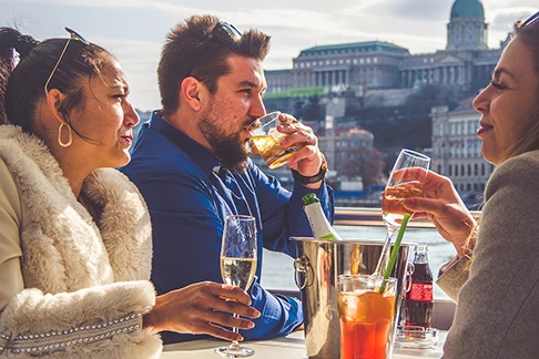 2 yung women and a bearded man drinking cocktail on a cruise boat in Budapest at daytime