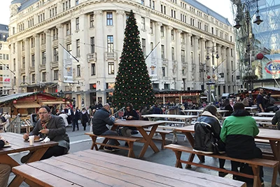 The eating out area with wooden tables and benches in Vörösmarty Square. The Xmas tree in the background on a cloudy winter morning