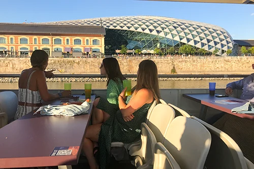 3 young ladies sitting on the open upper deck of a cruise ship, while sailing past the Whale building late in the afternoon in sumemr