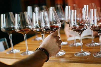 a hand reaching for a wine glass with some red wine in it, possibly on a wine tasting event