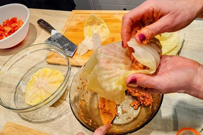 making stuffed cabbage rolls. photo is showing the stuffing - minced meat - being rolled into a sour cabbage leaf by a woman