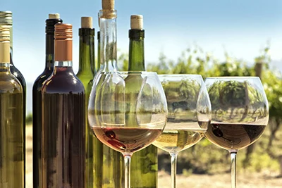 a couple of wine bottles with 3 glasses of wine next to them (rose, white and red wine in the glasses), a vineyard can be seen in the background