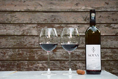 a bottle of Kolna red wine by Geza balla, and two wine glasses with red wine in them standing to the left of the bottle