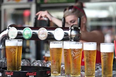 around 7 mugs of beer nex to each other in front of a beer tap, possibly on a beer festival