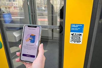 a hand holding a mobile phone and preparing to scan a public transport ticket on the door of a tram