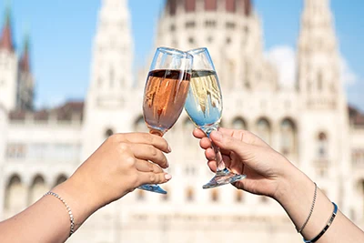 two people toasting with a glass of rose and white prosecco (only the hands holding the glasses can be seen, with the Parliament in the background