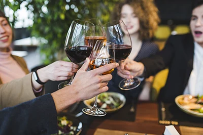 young men and woman toasting with glasses of red wine at a dinner table