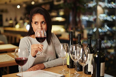 a young, dark-haired woman smelling red wine in a glass, possibly in a wine bar