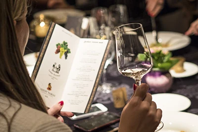 a young woman looking at a menu while holding a glass of white wine in her right hand in a restaurant