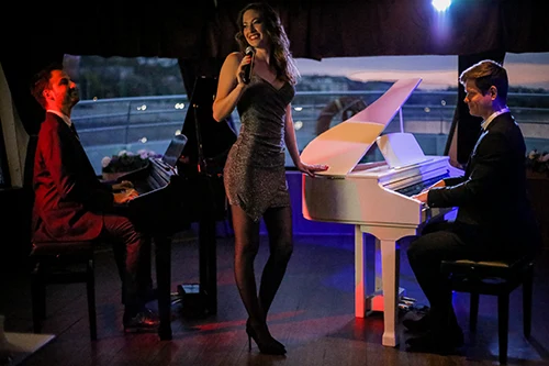 Two guys playing the piano and a young woman singing onboard the cruise ship at night