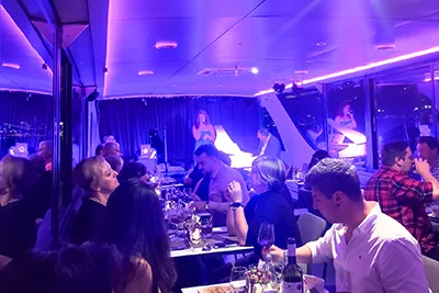 diners on a river cruise with dinner program - two pianists and a young female singer performing on the stage in the back of the room