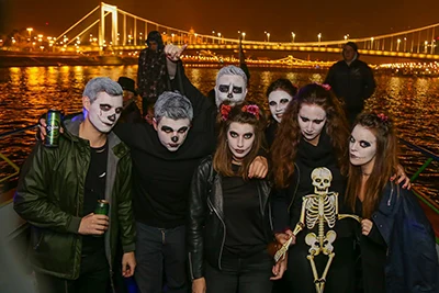 party people dressed in Halloween costume on board a cruise boat in Budapest, the illuminated Elizabeth bridge in the baclground